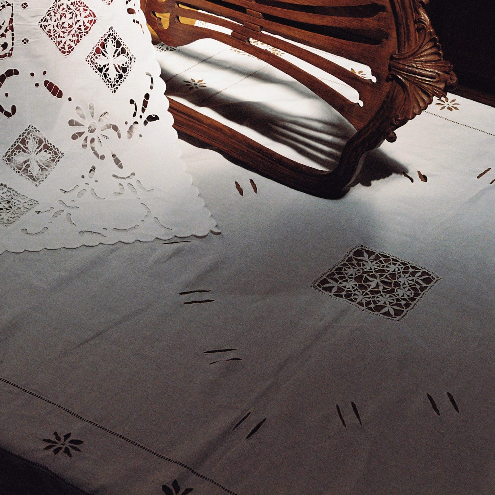 Portuguese lace and linen tablecloth photographed in warm interior light showing handmade craftsmanship. Vintage Portuguese tablecloth with lace trim and drawn-thread embroidery styled on wooden chair in natural light.