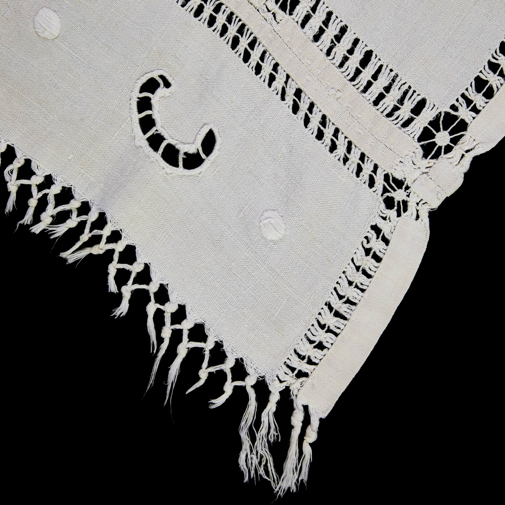 Close-up of white linen tablecloth showing openwork embroidery and hand-crocheted edge.